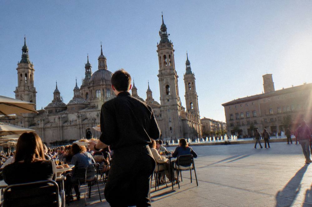 A waiter carrying small plates of tapas through a crowded bar in Zaragoza's old town