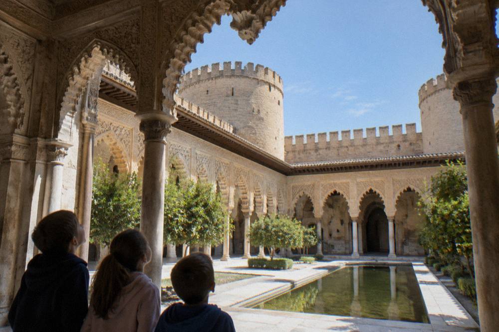 Children looking up at the ornate ceiling inside a Moorish palace courtyard with arches