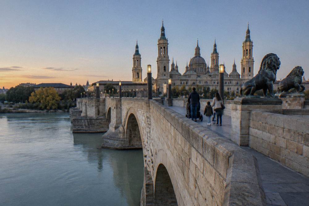 A family with a stroller crossing a historic stone bridge over a wide river at golden hour