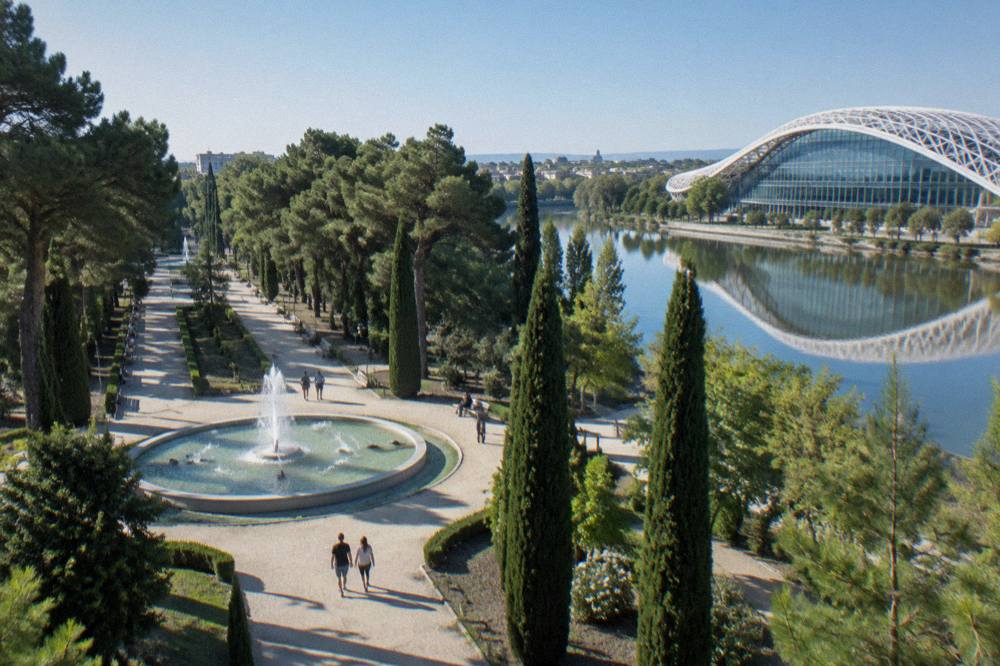 A glass building beside a river with a curved white lattice roof reflected in still water